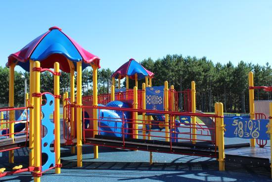 Image shows the Putnam Heights Neighborhood playground equipment displaying the wheel chair accessible ramp onto the play equipment. The ramp is a slow incline connecting several sections of the equipment, several sections feature overhead canopy. This is one of two playgrounds in the Eau Claire area providing wheel chair accessible ramps the support greater accessibility to engage with the playground equipment.